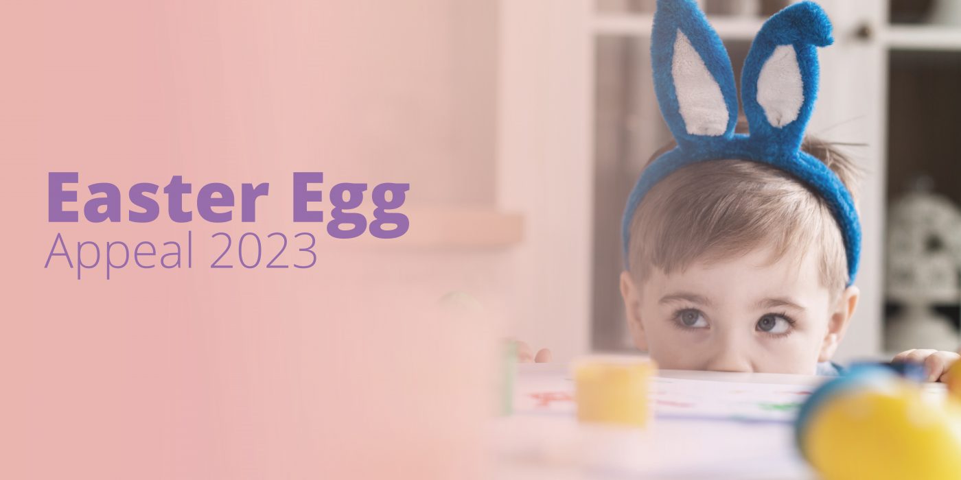 Easter Egg Appeal 2023, image shows a little boy with bunny ears hiding behind a table with chocolate eggs